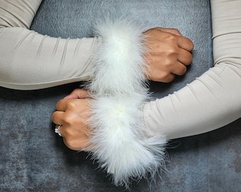 May include: Cream-colored sleeves with white feather cuffs. The cuffs are fluffy and add a touch of elegance. The sleeves are made of a soft material. The background is a dark gray.