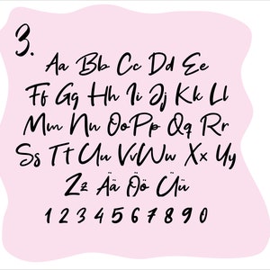 Op de afbeelding: Een roze achtergrond met een handgeschreven alfabet en cijfers in het zwart. Het alfabet bevat hoofdletters en kleine letters, evenals accentletters. De cijfers zijn 1 tot en met 9 en 0.