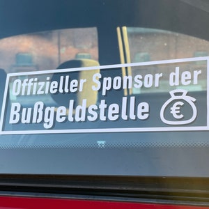 Könnte beinhalten: Ein weißer Aufkleber auf einer Autoscheibe mit der Aufschrift "Offizieller Sponsor der Bußgeldstelle" und einem Euro-Symbol in einem Geldbeutel.