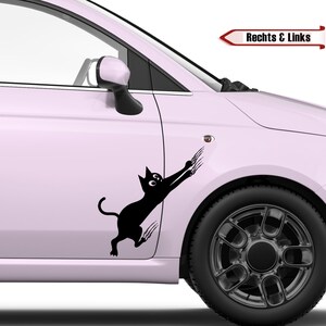 Könnte beinhalten: Ein schwarzer Katzenaufkleber mit ausgefahrenen Krallen ist an der Seite eines hellrosa Autos angebracht. Der Aufkleber befindet sich an der Fahrertür, direkt hinter dem Seitenspiegel. Das Auto hat schwarze Räder.