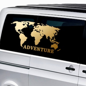 Könnte beinhalten: Ein goldener Weltkarten-Aufkleber mit dem Wort "ADVENTURE" darunter, auf der Heckscheibe eines silbernen Vans angebracht.