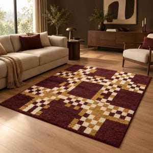 Puede incluir: Una alfombra rectangular con un color base burdeos intenso y un patrón geométrico prominente compuesto por cuadrados interconectados en tonos crema y amarillo mostaza, creando un diseño texturizado en forma de cuadrícula en toda la superficie.