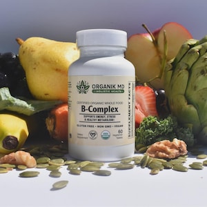 Peut inclure: Un flacon en plastique blanc de comprimés de complément alimentaire B-Complex Organik MD entouré de produits frais, dont un artichaut vert, une poire jaune, une banane, du brocoli, une tranche de citron vert, une carotte, une fraise et des noix.