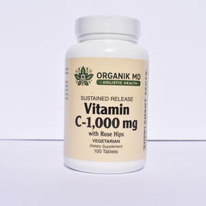 May include: A white bottle of Organik MD Vitamin C-1,000 mg tablets with rose hips. The label includes the text "Sustained Release" and "Vegetarian". The bottle contains 100 tablets.