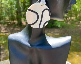May include: A pair of white and black statement earrings with a geometric design. The earrings are round and have a black and white abstract pattern.