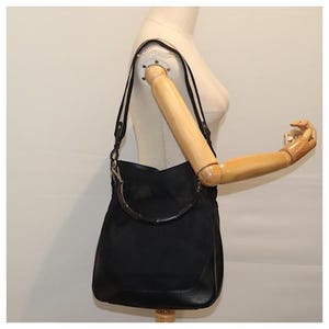 May include: A black canvas and leather shoulder bag with a brown leather handle.