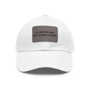 May include: White cotton baseball cap with a grey patch that reads "Let them throw shade. Use it to avoid sun damage."