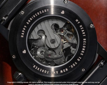 May include: Black watch with a clear back revealing the inner workings of the watch. The back of the watch is engraved with the text "MY HEART BELONGS TO YOU, NOW AND FOREVER. HAPPY ANNIVERSARY".
