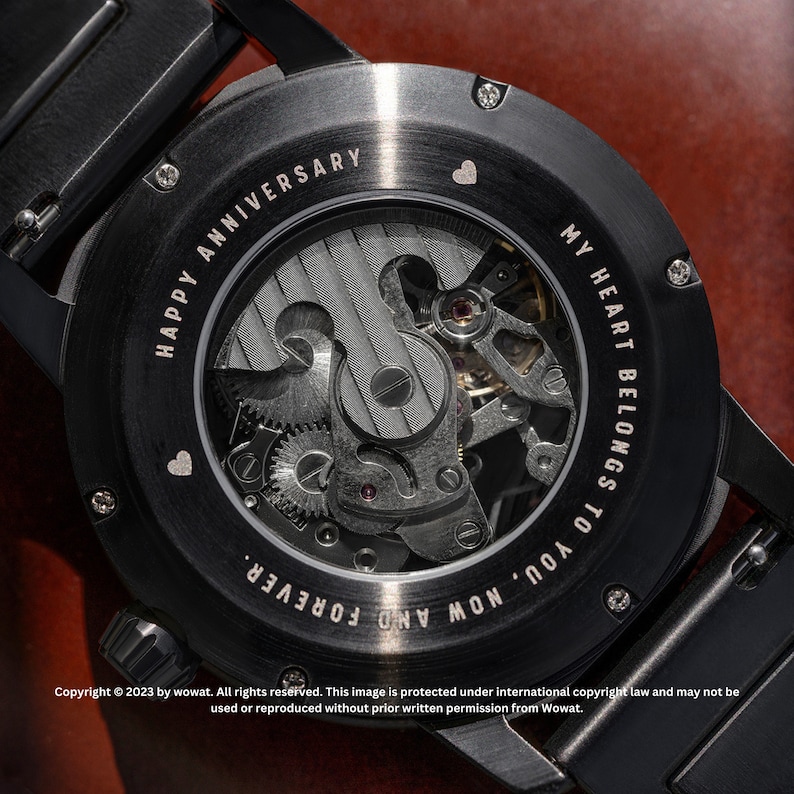May include: Black watch with a clear back revealing the inner workings of the watch. The back of the watch is engraved with the text "MY HEART BELONGS TO YOU, NOW AND FOREVER. HAPPY ANNIVERSARY".