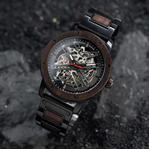 May include: A black and brown wristwatch with a skeleton dial and a wooden band. The watch face has the text "Original Design" printed on it.