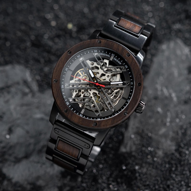 May include: A black and brown wristwatch with a skeleton dial and a wooden band. The watch face has the text "Original Design" printed on it.