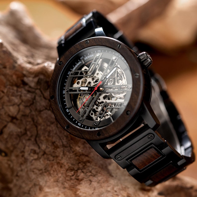 May include: A black wooden wristwatch with a black leather band and a clear face revealing the intricate mechanical workings of the watch. The watch face has white markings and a red second hand.