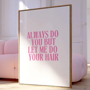 May include: A framed print with the text "ALWAYS DO YOU BUT LET ME DO YOUR HAIR" in pink lettering. The print is in a gold frame and stands on a wooden floor. A pink sofa is in the background.