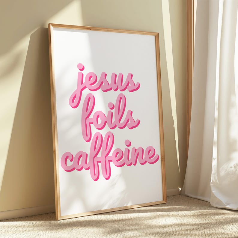K&ouml;nnte beinhalten: Ein gerahmter Kunstdruck mit dem Schriftzug "jesus foils caffeine" in rosa Schrift. Die W&ouml;rter haben einen Schatteneffekt, und der Druck befindet sich in einem hellen Holzrahmen. Der Hintergrund ist wei&szlig;.