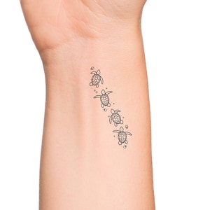 May include: A close-up of a person's wrist with a temporary tattoo of five small sea turtles swimming in a line.