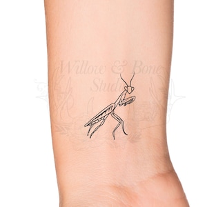 May include: A black line art tattoo design of a praying mantis on a person's wrist.