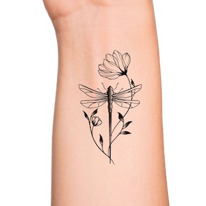 May include: A black line drawing tattoo design of a dragonfly with wings spread, perched on a stem with two flowers.