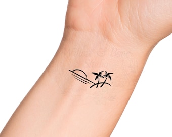 May include: A black line drawing tattoo of two palm trees and a setting sun on a person's wrist.