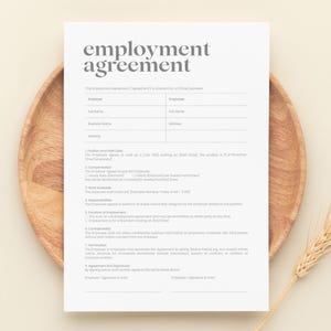 May include: A white employment agreement form titled "employment agreement" in a serif font. The form is on a wooden plate with a wheat stalk on a beige background. The form includes fields for employee and employer details.
