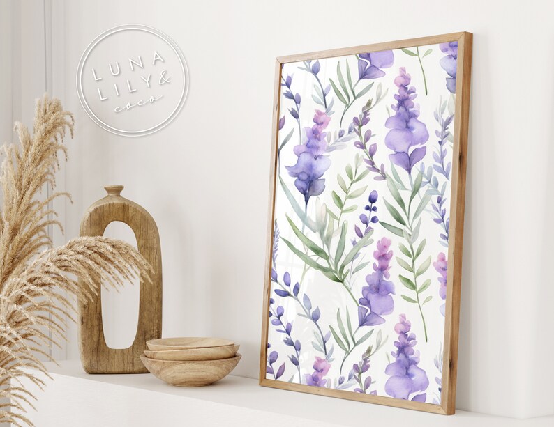 Op de afbeelding: Een ingelijst print met een aquarelpatroon van paarse en groene bloemen op een witte achtergrond. De lijst is van lichtbruin hout.
