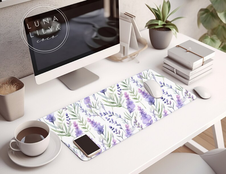 Op de afbeelding: Een wit bureau met een computermonitor, een kopje koffie, een potplant, een stapel boeken, een witte muis, een smartphone en een lavendelbloem muismat met de tekst "LUNA LILY & coco".
