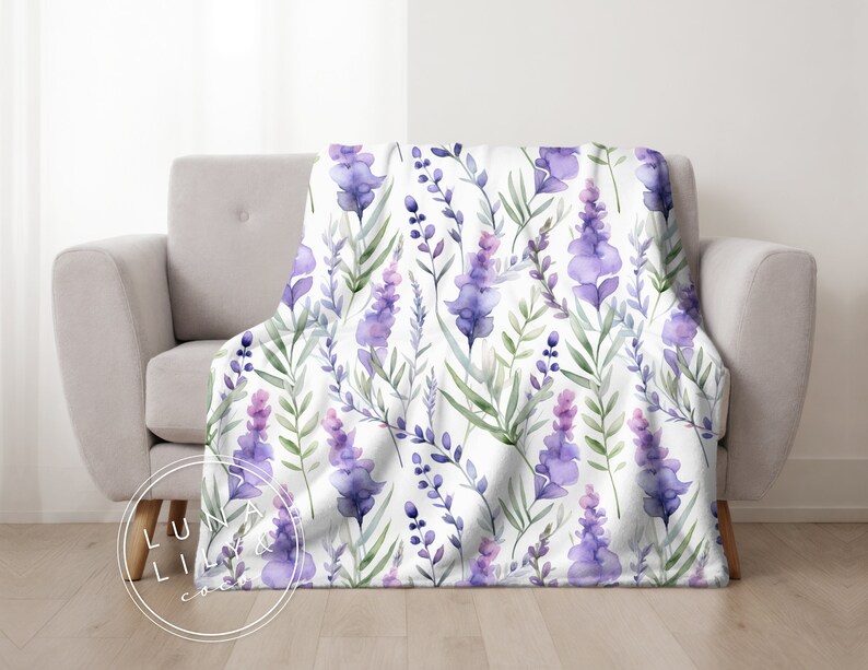 Op de afbeelding: Een witte deken met een lavendelbloemenpatroon. De deken heeft aquarel-achtige paarse en groene lavendelbloemen op een witte achtergrond.