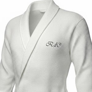 May include: White waffle-weave dressing gown with a shawl collar. The gown has an embroidered "RdC" monogram on the chest. The robe is made of a textured fabric and has a classic, comfortable design.