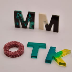 May include: A set of colourful letters spelling out "MOTK" with a red and white ring in the centre. The letters are made of clear acrylic with different colours and patterns.