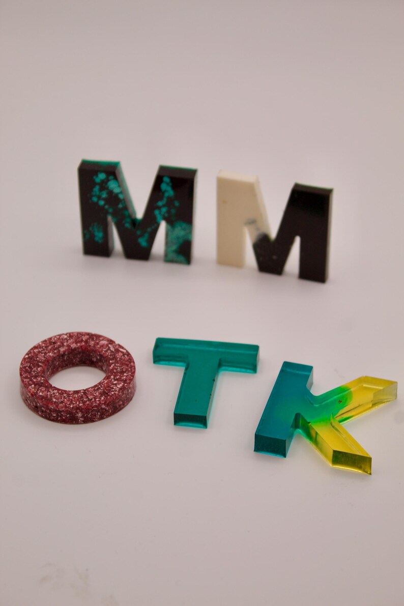 May include: A set of colourful letters spelling out "MOTK" with a red and white ring in the centre. The letters are made of clear acrylic with different colours and patterns.