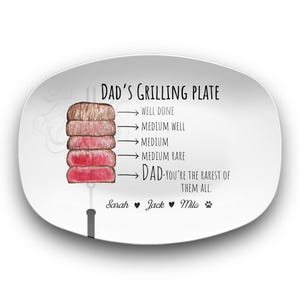 May include: White ceramic serving plate with a graphic of a steak and a thermometer showing different levels of doneness. The text "DAD'S GRILLING PLATE" is at the top of the plate. The text "DAD-YOU'RE THE RAREST OF THEM ALL." is below the graphic. The names "Sarah", "Jack", and "Mila" are at the bottom of the plate.
