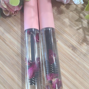 May include: Two clear glass bottles with pink caps filled with a clear liquid and dried rose petals. The bottles have a black mascara wand inside.
