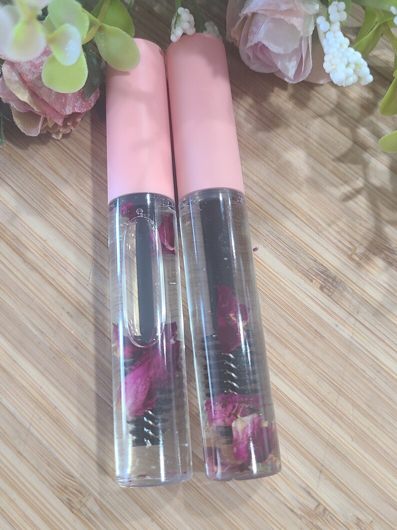May include: Two clear glass bottles with pink caps filled with a clear liquid and dried rose petals. The bottles have a black mascara wand inside.