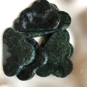 May include: A group of six green agate heart-shaped stones in a white bowl. The stones have a cloudy, mottled appearance.