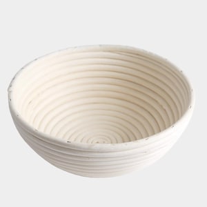 May include: A round, off-white banneton proofing basket with a spiral pattern. The basket is made of woven material and is designed for proofing bread dough. The interior features concentric circles, creating a textured surface for the dough.