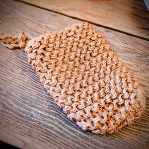May include: A close-up of a brown knitted pouf or bath scrubber made of natural fibers. The pouf is textured and has a rough surface.