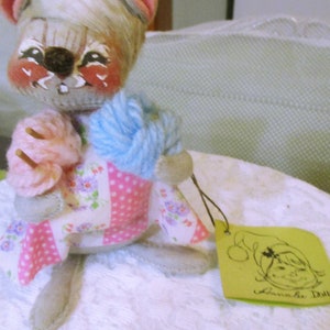 May include: A white and pink plush toy mouse wearing a pink and white polka dot dress and holding blue and pink yarn. The mouse has painted facial features and is holding a knitting needle. The toy is labeled "Annabelle Doll".