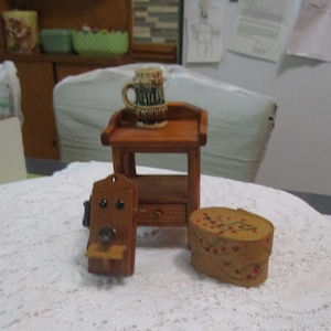 May include: A miniature wooden table with a shelf and a drawer, a small wooden wall phone, a wooden box with red and green painted flowers, and a brown and white ceramic mug.