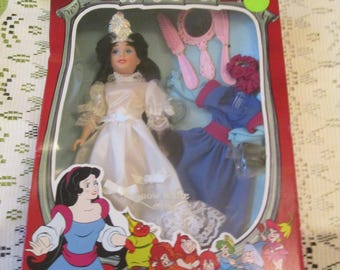 May include: A vintage Snow White doll in a red box. The doll is wearing a white dress and has black hair. The box includes accessories and a second blue dress. The box reads "Happily Ever After".