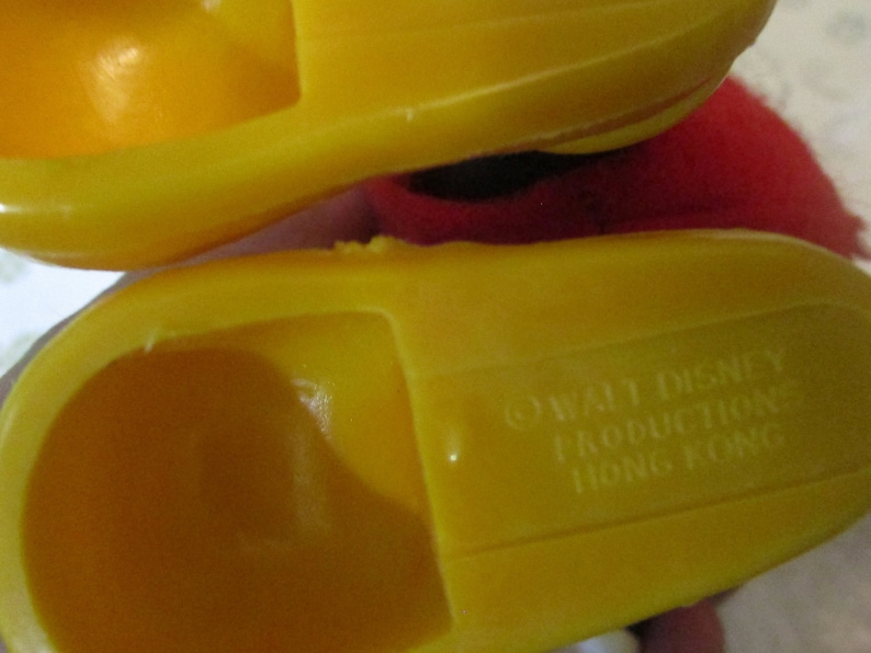 May include: Close-up of two yellow plastic toy shoes. The underside of one shoe is visible, with the text "&copy; WALT DISNEY PRODUCTION HONG KONG" embossed. The shoes are a bright, solid yellow colour.