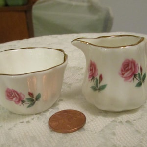 May include: A white porcelain creamer and sugar bowl set with a gold trim and pink rose floral pattern.