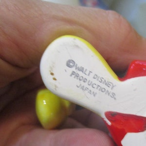 May include: Close-up of the bottom of a ceramic figurine. The figurine is yellow and red. The bottom is white with the text "&copy; WALT DISNEY PRODUCTIONS JAPAN" printed on it.
