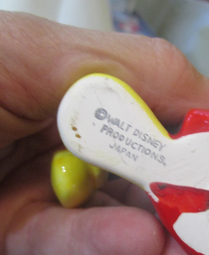 May include: Close-up of the bottom of a ceramic figurine. The figurine is yellow and red. The bottom is white with the text "&copy; WALT DISNEY PRODUCTIONS JAPAN" printed on it.