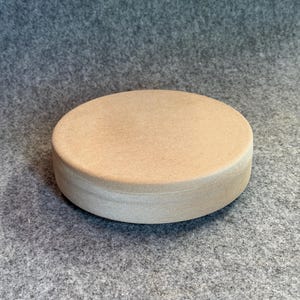 Könnte beinhalten: Ein kreisförmiges Objekt mit flacher Oberseite, einer glatten, hellbeigen Oberfläche und einem dicken, zylindrischen Seitenprofil. Der Gegenstand weist eine gleichmäßige, matte Textur auf und zeigt eine einfache, solide und schmucklose geometrische Form.