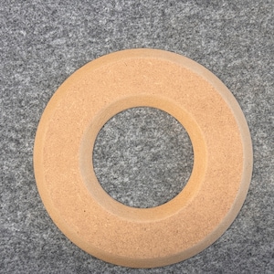 Peut inclure: Un anneau rond en bois de couleur brun clair avec un grand trou au centre. L'anneau est fait d'un matériau texturé et a une surface légèrement rugueuse.
