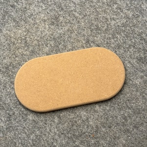 Könnte beinhalten: Ein ovaler Untersetzer aus hellem Holz. Der Untersetzer ist glatt und hat eine leicht raue Textur.