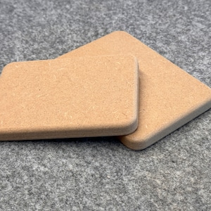 Könnte beinhalten: Zwei quadratische, braune Untersetzer aus Pappe. Die Untersetzer sind aus einem strukturierten Material gefertigt und haben abgerundete Kanten.