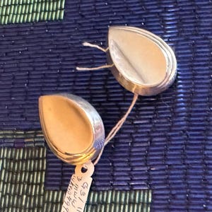 May include: A pair of silver teardrop-shaped earrings with a smooth, polished finish. The earrings are connected by a thin, white string.
