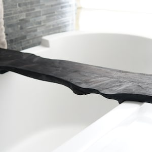 Peut inclure: Un plateau de bain en bois noir avec un bord naturel posé sur le bord d'une baignoire blanche.