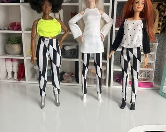 May include: Three fashion dolls wearing black and white checkered leggings. The doll on the left is wearing a neon green tank top, the doll in the middle is wearing a white long-sleeved shirt, and the doll on the right is wearing a black and white polka dot shirt with black sleeves.