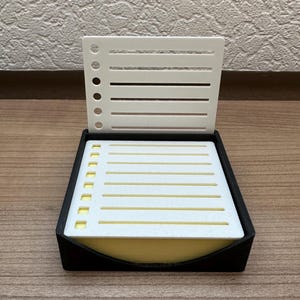 Könnte beinhalten: Eine schwarze Fliegenfischbox mit einem weißen Schaumstoffeinsatz und einem weißen Deckel mit einem Gittermuster. Der Deckel ist geöffnet und der Schaumstoffeinsatz ist sichtbar.